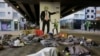 Para tunawisma tidur di bawah jembatan di depan mural yang menggambarkan Presiden A. Donald Trump sebagai dalang yang memanipulasi Presiden Brasil Jair Bolsonaro, di pusat kota Sao Paulo, Brasil, 23 Juli 2019. (Foto: AP)