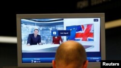 FILE - A trader works in front of a news broadcast on a TV at the stock exchange in Frankfurt.