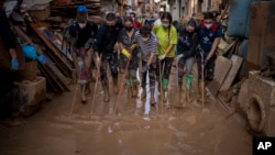 Relawan dan warga membersihkan kubangan lumpur dari jalanan di daerah yang terdampak banjir di Paiporta, Valencia, Spanyol timur. 