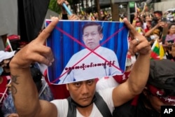 Seorang warga negara Myanmar yang tinggal di Thailand memegang foto Jenderal Senior Min Aung Hlaing, Kepala Dewan Militer, saat demonstrasi di luar Kedutaan Myanmar di Bangkok, Thailand, Selasa, 26 Juli 2022. (Foto: AP)