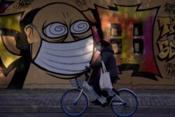 A woman wearing a protective mask cycles past a graffiti-painted wall at a construction site in Shanghai, China, as the country is hit by coronavirus outbreak, Feb. 17, 2020.