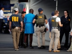 Federal agents hold a detainee, second from left, in downtown Los Angeles after predawn raids that saw dozens of people arrested in the L.A. area, Aug. 22, 2019, Most of the defendants are Nigerian nationals.