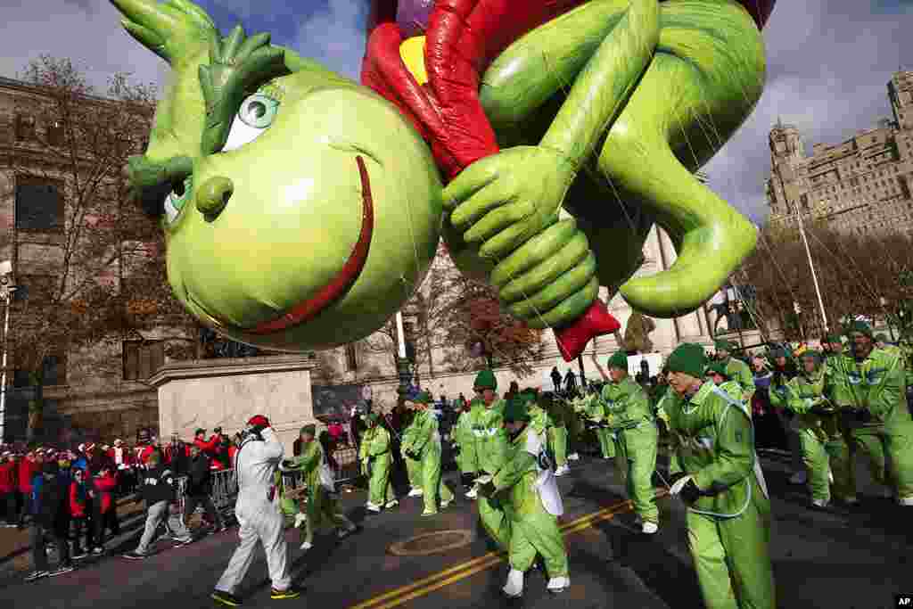 Los manipuladores de globos sostienen el Grinch del Dr. Seuss cerca del suelo mientras los fuertes vientos afectan el desfile.