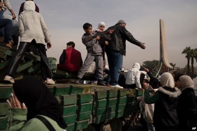 A boy holding a rifle borrowed from a Syrian opposition fighter poses on the top of a government forces tank that was left on a street, at the Umayyad Square in Damascus, Syria, Dec. 11, 2024.