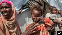 FILE - Nasteho Hassan Mohyadin, 3, and her mother Farhid Ali Mohamed sit outside their small makeshift tent in a camp for those displaced by 2012 famine or by conflict, in Mogadishu, Somalia.