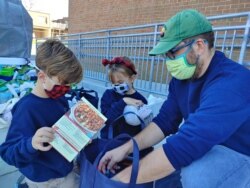 Foster Marchand helps his father, Sterling, pack a bag with Thanksgiving food items for low income families at Mount Vernon Woods Elementary School in Alexandria, Virginia. (Deborah Block/VOA)