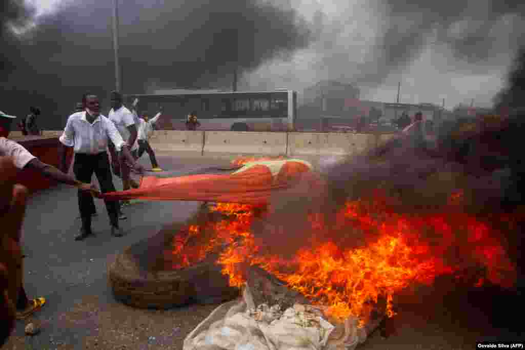 Manifestantes queimam a bandeira do MPLA durante a manifesta&#231;&#227;o contra o governo. A pol&#237;cia anti-motim, alguns montados em cavalos, disparou g&#225;s lacrimog&#233;neo e agrediu dezenas de manifestantes que tomaram as ruas da capital angolana. 24 outubro 2020