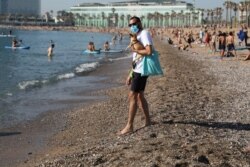 A man wearing a protective face mask carries a dog as he enjoys the sunny weather at Barceloneta beach, amid the coronavirus disease (COVID-19) outbreak, in Barcelona, Spain, May 21, 2020