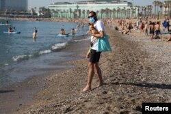 A man wearing a protective face mask carries a dog as he enjoys the sunny weather at Barceloneta beach, amid the coronavirus disease (COVID-19) outbreak, in Barcelona, Spain, May 21, 2020