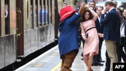 Britain's Catherine, Duchess of Cambridge, (C) dances with a person in a Paddington Bear outfit by her husband Britain's Prince William, Duke of Cambridge as they attend a charities forum event at Paddington train station in London on October 16, 2017.