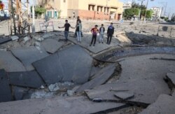 Palestinian youths take pictures with their smart phones of a huge crater on a main road in Gaza City on May 13, 2021 following continued Israeli airstrikes overnight on the Hamas-controlled Gaza Strip.