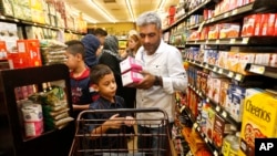 Nadim Fawzi Jouriyeh, a Syrian refugee who arrived recently in the United States with his wife and four children, puts items in a cart while shopping with his son, Farouq Nadim Jouriyeh, in El Cajon, Calif., Aug. 31, 2016.