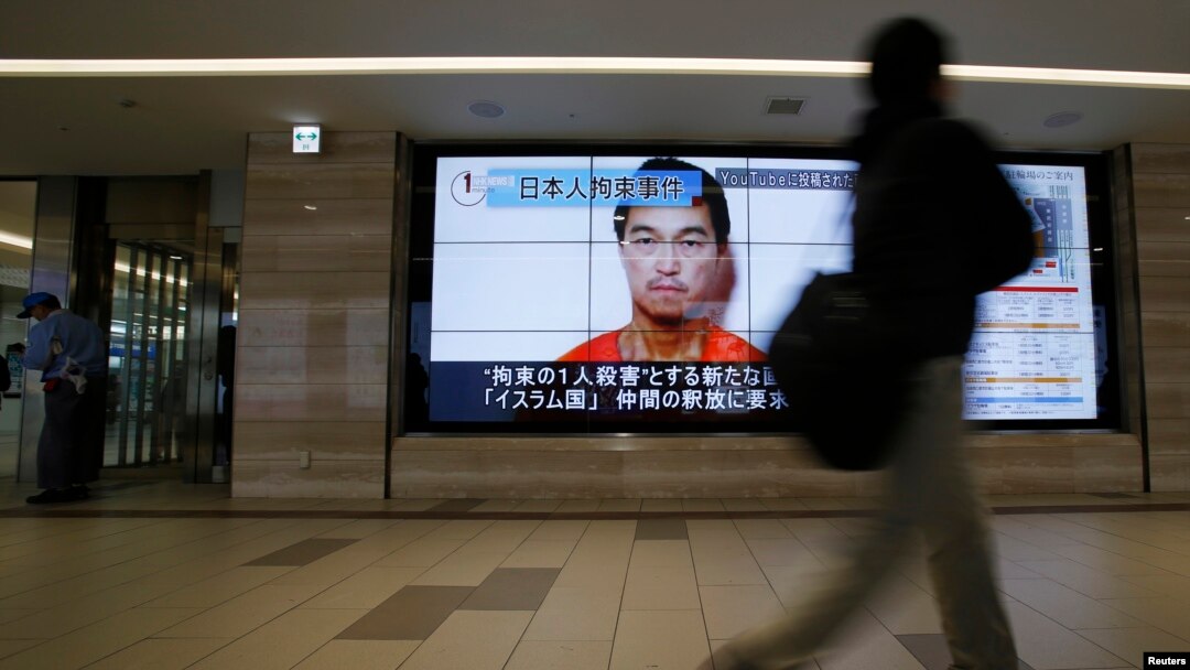 Seseorang di Tokyo berjalan melewati layar televisi yang menayangkan wajah sandera ISIS dari Jepang, Kenji Goto.