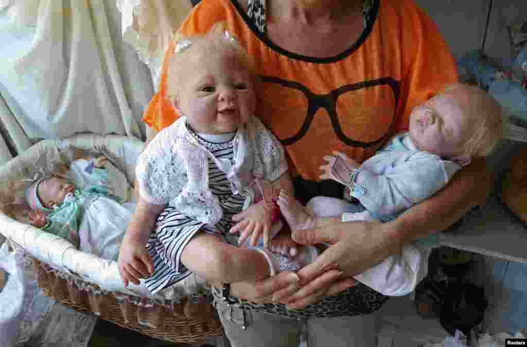 Seniman Belgia Beatrice Van Landeghem berpose dengan dua boneka &quot;Bayi yang Lahir Kembali&quot; yang dinamai&nbsp; Sofia (kiri) dan Loan (kanan), di bengkel seninya&nbsp; &#39;La nurserie des Tis Lous De Bea&#39; di La Louviere, Belgia Selatan (8/8). Biaya pembuatan &quot;bayi-bayi&quot; tersebut bervariasi antara ratusan hingga ribuan Euro dan memakan waktu sekitar 25 jam untuk membuatnya tergantung pada tingkat kesukaran yang diminta oleh orang-orang yang &#39;mengadopsi&#39; boneka-boneka itu.