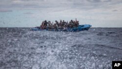 FILE - Men from Morocco and Bangladesh react on an overcrowded wooden boat, as aid workers of the Spanish NGO Open Arms approach them in the Mediterranean Sea, international waters, off the Libyan coast, Jan. 10, 2020.