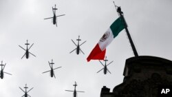 FILE - Military helicopters fly past the Mexican flag atop the National Palace, during the annual Independence Day military parade in Mexico City's main square, Sept. 16, 2016.