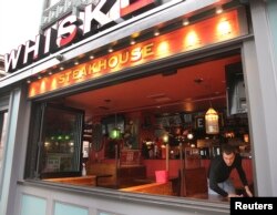 Pegawai Alec Mikels membersihkan meja di restoran Whiskey's Smokehouse di Boylston Street, Boston, sebelum tempat itu buka kembali pada 23 April.