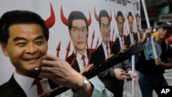 FILE - A protester raises a poster depicting outgoing Chief Executive Leung Chun-ying, left, with devil horns during a rally on the first day of 2017 in Hong Kong, Jan. 1, 2017.