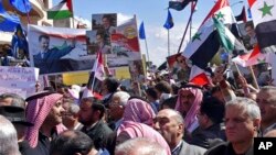 In a photo released by Syrian official news agency SANA, Syrians hold national flags and portraits of Syrian President Bashar Assad during a protest against President Donald Trump's move to recognize Israeli sovereignty over the occupied Golan Heights, in Homs, March 26, 2019.