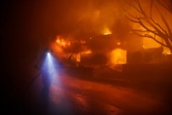 A firefighters gets in position to hose down flames as a home burns in the Getty fire area along Tigertail Road, Oct. 28, 2019, in Los Angeles.