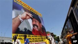 Sri Lankans walk past a billboard of President Mahinda Rajapaksa and campaign slogans for people to join the protest against the U.N. report, Colombo, Apr 21 2011