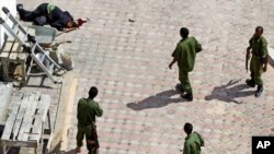 Sojojin Somaliya su na tsaye kusa da gawar wani da aka ce ma'aikacin hotel din ne a hagu, wanda ya mutu bayan tashin bama-bamai biyu a kusa da kofar shiga hotel din mai suna Jazeera Palace, hedkwatar wucin-gadi ta sabon shugaban Somaliya, Hassan Sheikh Mohamud.