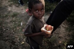 Seorang anak laki-laki berjalan setelah menerima distribusi makanan dari supermarket lokal di pusat evakuasi di Dondo, sekitar 35 km sebelah utara Beira, Mozambik, pada 27 Maret 2019. (Foto: AFP)