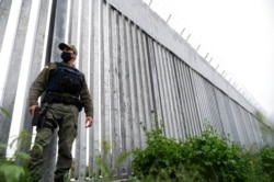 FILE - A policeman patrols alongside a steel wall at Evros River, near the village of Poros, at the Greek -Turkish border, Greece, May 21, 2021.