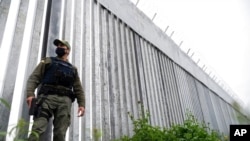 FILE - A policeman patrols alongside a steel wall at Evros River, near the Greek village of Poros, at the Greek-Turkish border, May 21, 2021.