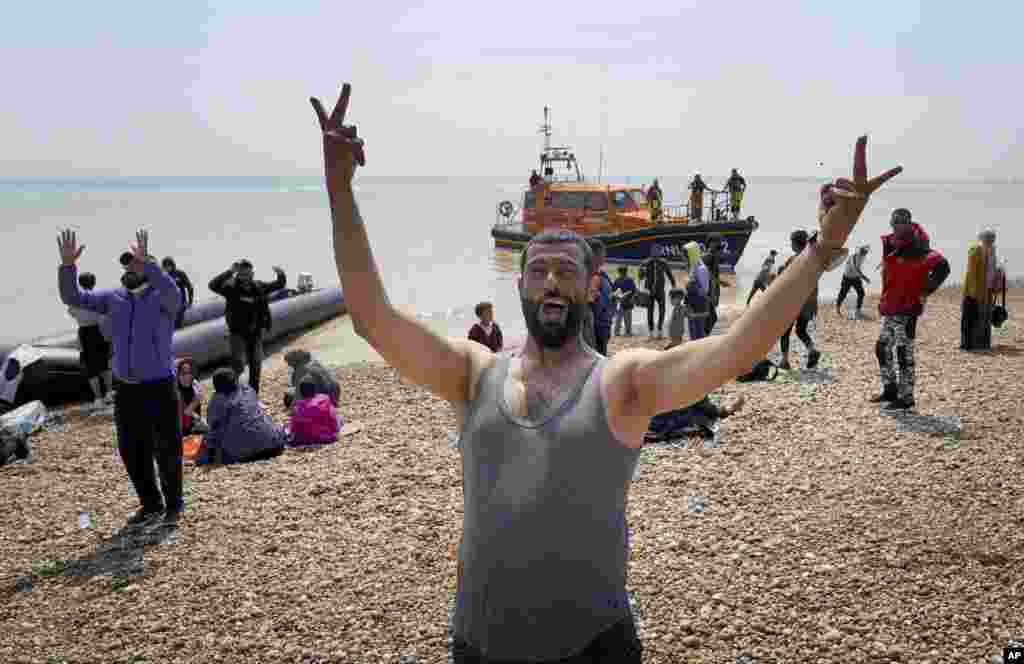 A man gestures as people thought to be migrants stand on the beach after arriving on a small boat at Dungeness in Kent, England.