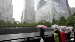 Orang-orang berdiri dengan payung di Tugu Peringatan 9/11 di New York, Jumat, 9 Agustus 2024. (Foto: AP/Pamela Smith)