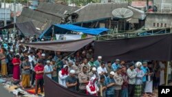 Muslim men perform Friday prayer as houses ruined by Sunday's earthquake are seen in the background at a makeshift mosque in Pamenang, Lombok Island, Indonesia, Aug. 10, 2018.