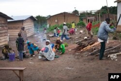 FILE - A man cuts wood as women prepare a meal in the camp for Central African refugees in Garoua Boulai, on the Cameroonian side of the border with the Central African Republic, April 28, 2014.