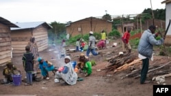 FILE - A man cuts wood as women prepare a meal in the camp for Central African refugees in Garoua Boulai, on the Cameroonian side of the border with the Central African Republic, April 28, 2014.