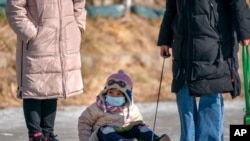 FILE - A child wearing a face mask to protect against the spread of the coronavirus is pulled in a sled across the surface of a frozen canal in Beijing, Jan. 30, 2021.