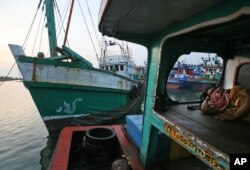 FILE - Seorang nelayan tidur di kapalnya saat kapal (kiri) yang digunakan untuk membawa Muslim Rohingya dari Myanmar dan migran dari Bangladesh berlabuh di sebuah pelabuhan di Lhokseumawe, provinsi Aceh, 14 Mei 2015. (Binsar Bakkara/AP)