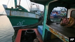 A fisherman sleeps on his boat as the vessel, left, used to carry Rohingya Muslims from Myanmar and migrants from Bangladesh is docked at a port in Lhokseumawe, Aceh province, Indonesia, May 14, 2015.