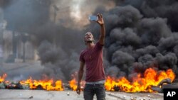 A protester takes a selfie at a burning barricade set by protesters in Port-au-Prince, Haiti, Oct. 18, 2021.