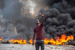 A protester takes a selfie at a burning barricade set by protesters in Port-au-Prince, Haiti, Oct. 18, 2021.