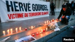 FILE - A man places a candle near a banner as people pay tribute to Herve Gourdel, a French mountain guide who was beheaded by an Algerian Islamist group, in Lyon, France, Sept. 26, 2014.