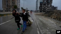 ARCHIVO - Niños tiran de un carro cargado de chatarra recogida de los escombros de los edificios destruidos en Antakya, en el sur de Turquía, el 12 de enero de 2024, casi un año después de que un poderoso terremoto devastara partes del país el 6 de febrero de 2023. 