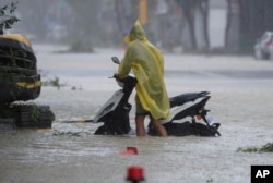 Un hombre empuja una motocicleta por una carretera inundada mientras el tifón Krathon toca tierra en Kaohsiung, sur de Taiwán, el 3 de octubre de 2024.