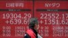 A man walks past an electronic stock board showing Japan's Nikkei 225 and New York Dow index at a securities firm in Tokyo Friday, March 27, 2020. Shares are mostly higher in Asia after stocks surged again on Wall Street with the approaching…