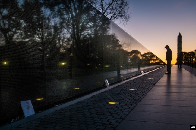 FILE - A visitor pauses at the Vietnam War Memorial in Washington early in the morning on Veterans Day, Monday, Nov. 11, 2013 to look at the names inscribed on the wall. The Washington Monument is at right. (AP Photo/J. David Ake, File)