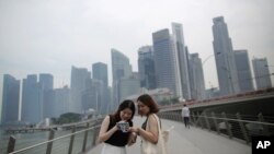 Tourists look at photographs taken on their smartphones in front of a hazy financial skyline in Singapore on Friday, Aug. 26, 2016.