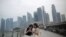 Tourists look at photographs taken on their smartphones in front of a hazy financial skyline in Singapore on Friday, Aug. 26, 2016.