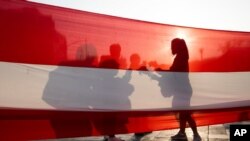 Demonstrators are silhouetted on a Peruvian flag before a march to demand significant social changes and a new constitution from the government of new interim president Francisco Sagasti in Lima, Peru, Nov. 18, 2020. 
