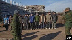 FILE - Ukrainian prisoners of war stand as Russia-backed separatists watch in front of the destoryed airport building outside Donetsk, Ukraine, Feb. 25, 2015.