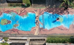 Foto udara ini memperlihatkan seorang perempuan (kanan) sedang memotret anak-anaknya (tengah) pada lukisan tiga dimensi sepanjang 300 meter, karya enam belas seniman dari Komunitas Perupa Jakarta yang melambangkan ekspresi dan semangat seniman di tengah pandemi COVID-19 di luar museum Basoeki Abdullah di Jakarta, 27 Agustus 2020. (ADEK BERRY / AFP)