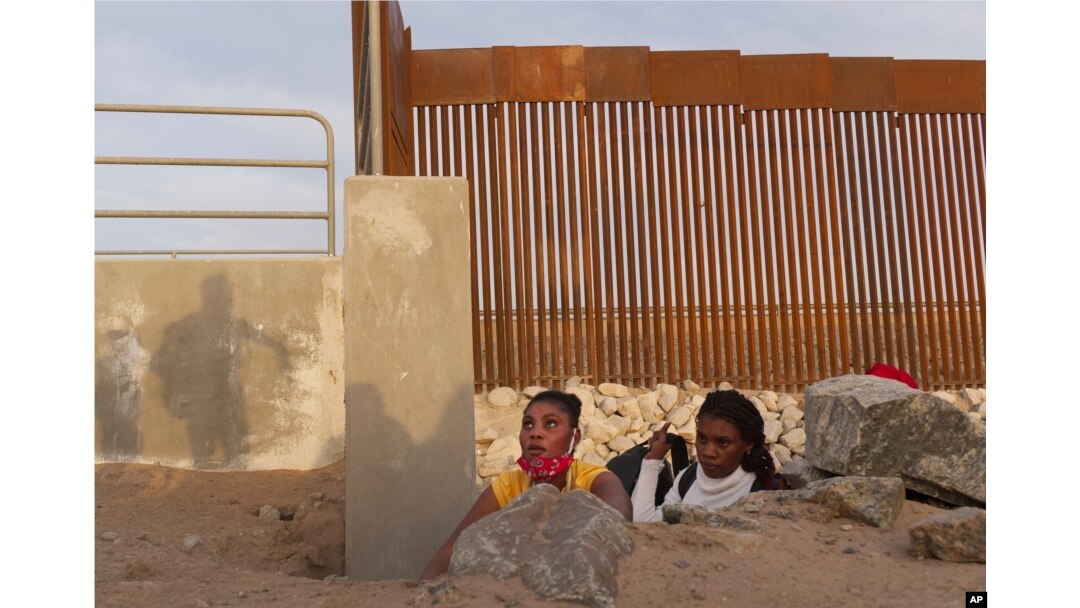 FILE - A Haitian migrant family looks to emerge from a rocky canal adjacent to a gap in the U.S. border wall in Yuma, Arizona, June 9, 2021.